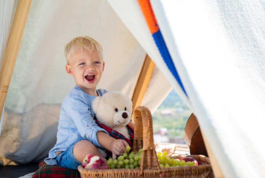 exciting toddler with a teddy bear and getting some grapes from a basket inside of a tent