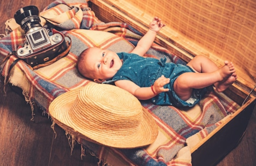 smiling baby laying in a vintage suitcase with a hat and a vintage camera