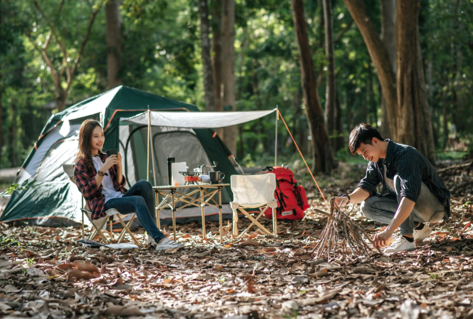 Young mand preparing preparing a pile of firewood for fire camping and pretty girl friend sitting at front of camping tent