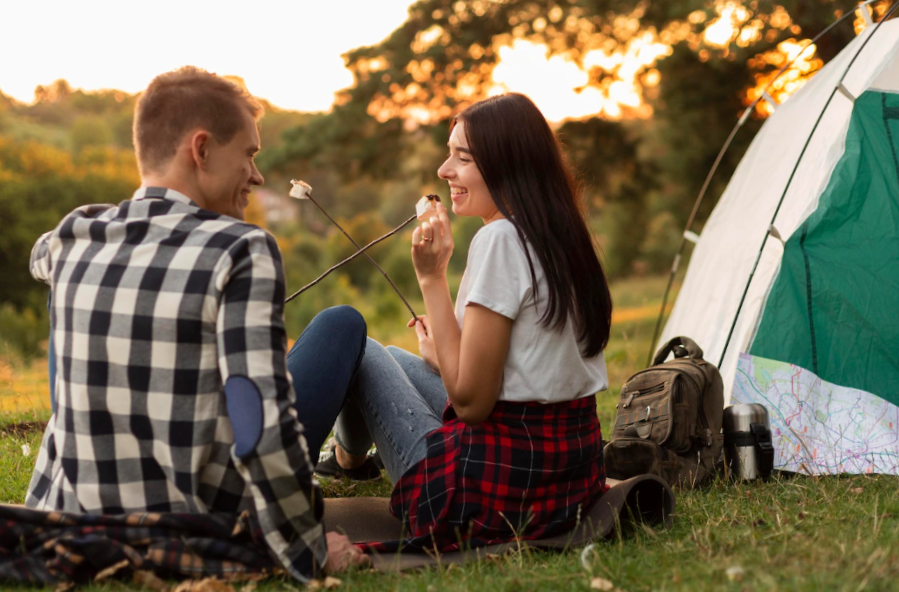 Back view young couple enjoying nature and cooking marshmallows together